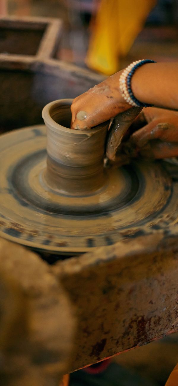 Clay-covered hands throwing a small cup on a potter’s wheel.