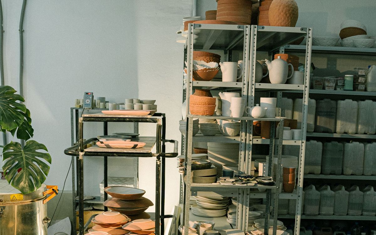 Metal shelves stacked with terracotta bowls, white jugs and plates in a pottery studio.
